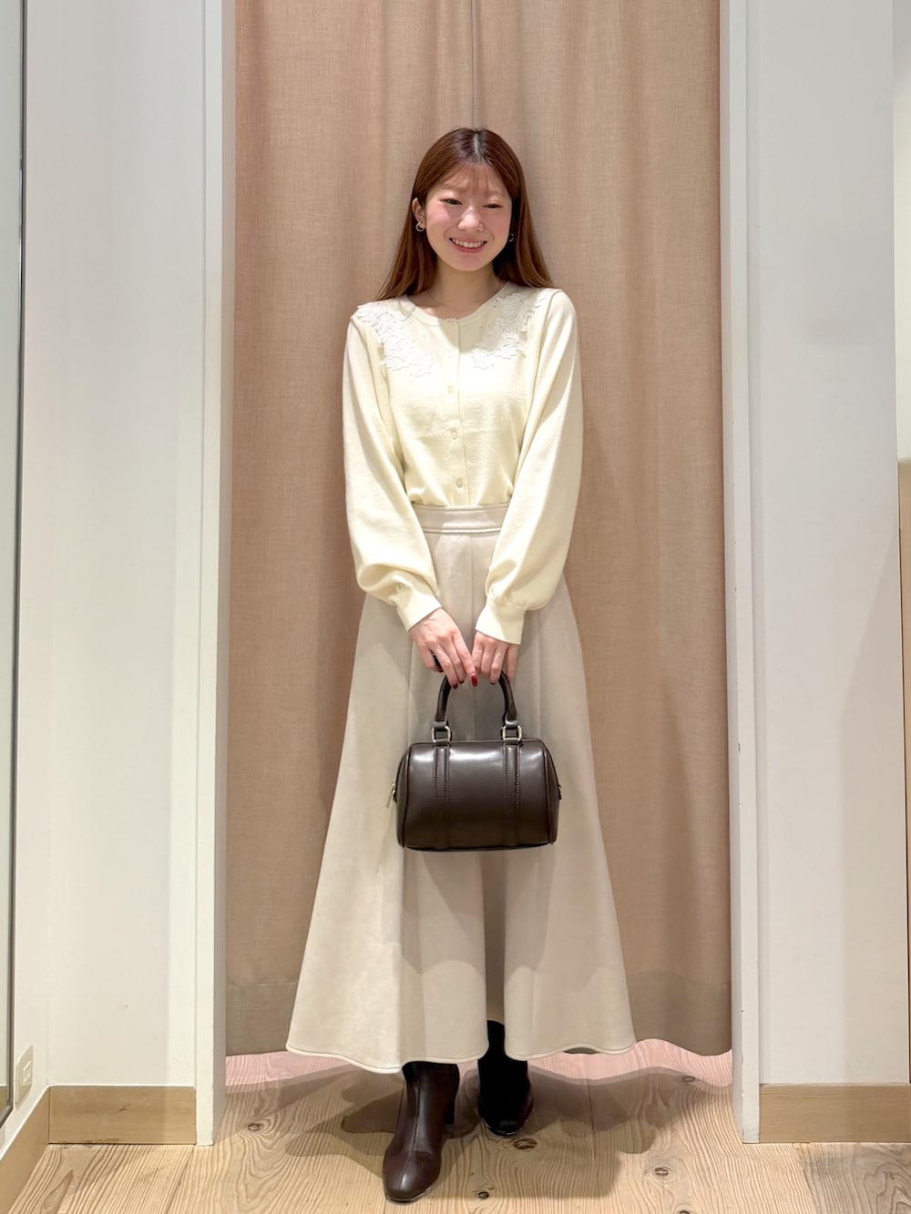 ホワイト系のカーディガン/ボレロ、ブラウン系のボストンバッグ、ベージュ系のスカートを着用したレディースの秋コーディネートの3枚目の写真