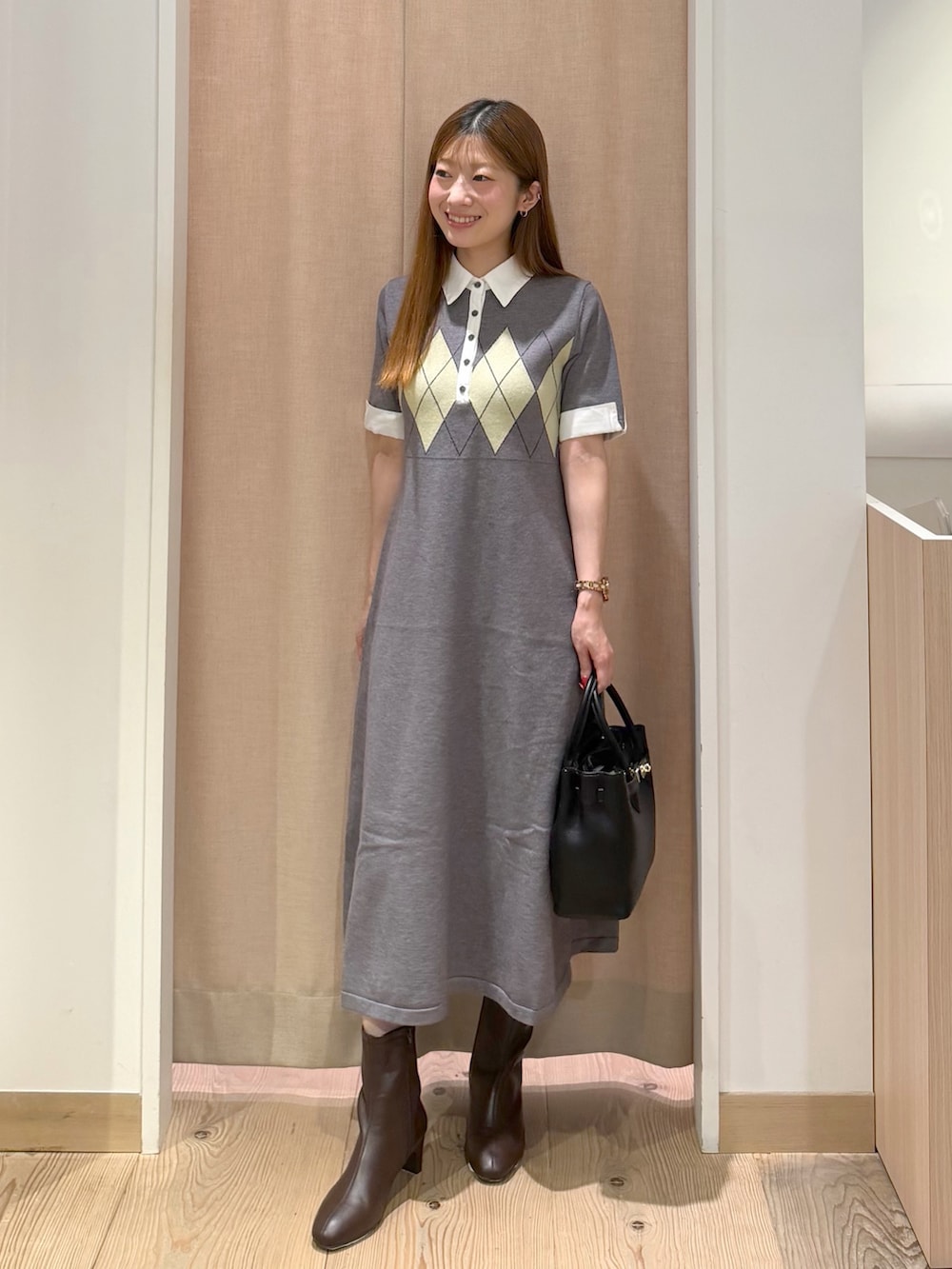 グレー系のワンピース、ブラック系のトートバッグ、ブラウン系のブーツを着用したレディースの秋コーディネートの2枚目の写真