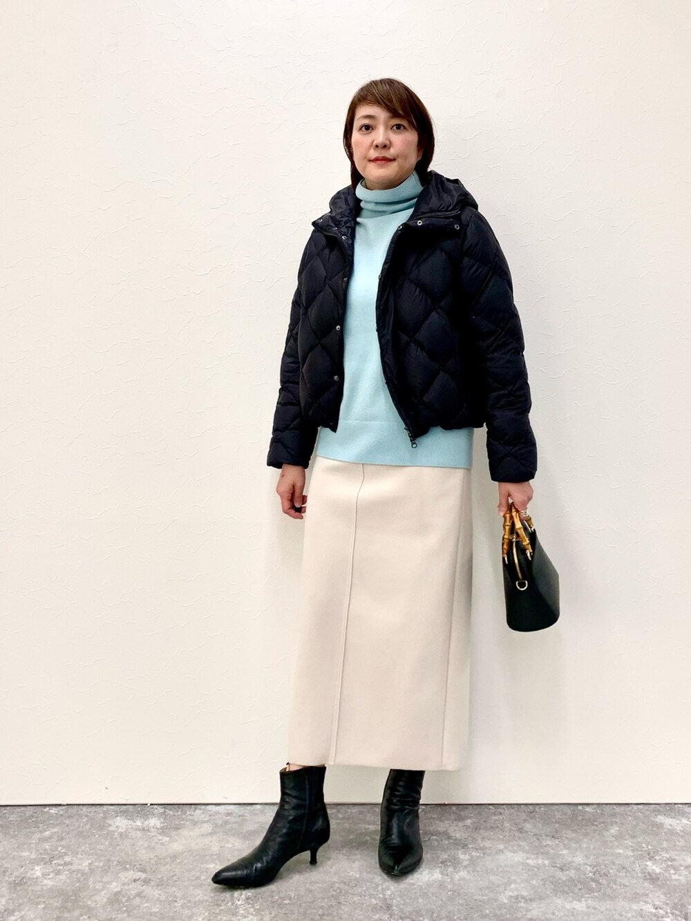ブラック系のショルダーバッグ、ベージュ系のスカート、ブラック系のダウンジャケット/コートを着用したレディースの冬コーディネートの2枚目の写真
