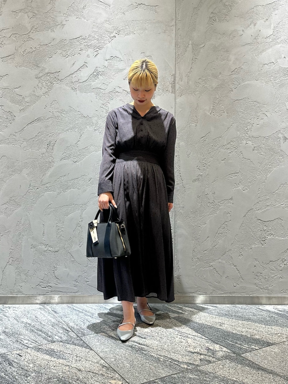 グレー系のワンピース、ブラック系のハンドバッグ、シルバー系のパンプスを着用したレディースの春コーディネートの2枚目の写真