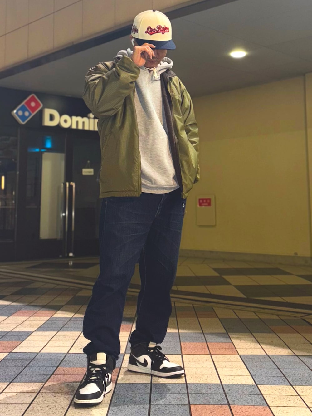 グリーン系のナイロンジャケット、グレー系のパーカー、ブルー系のデニムパンツを着用したメンズの冬コーディネートの2枚目の写真