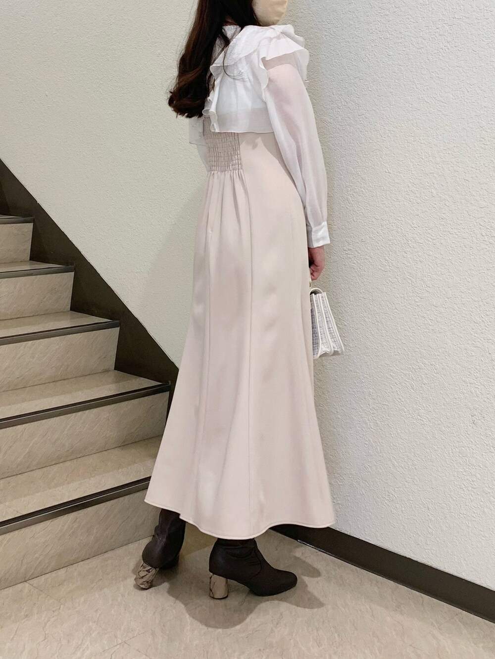 ブラウン系のブーツ、ベージュ系のワンピース、ホワイト系のハンドバッグを着用したレディースの冬コーディネートの2枚目の写真