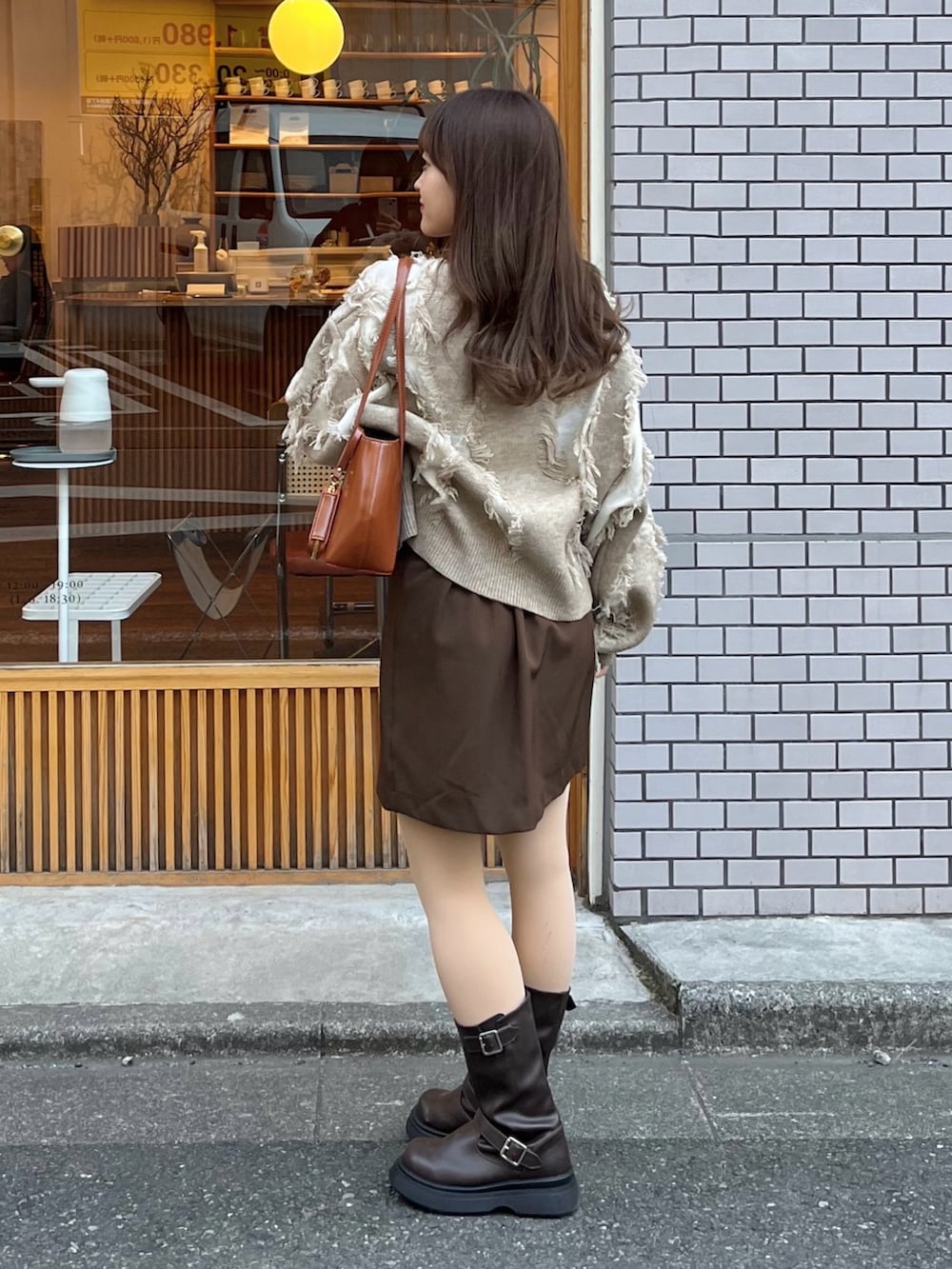 ブラウン系のスカート、ベージュ系のニット/セーター、ブラウン系のハンドバッグを着用したレディースの春コーディネートの2枚目の写真