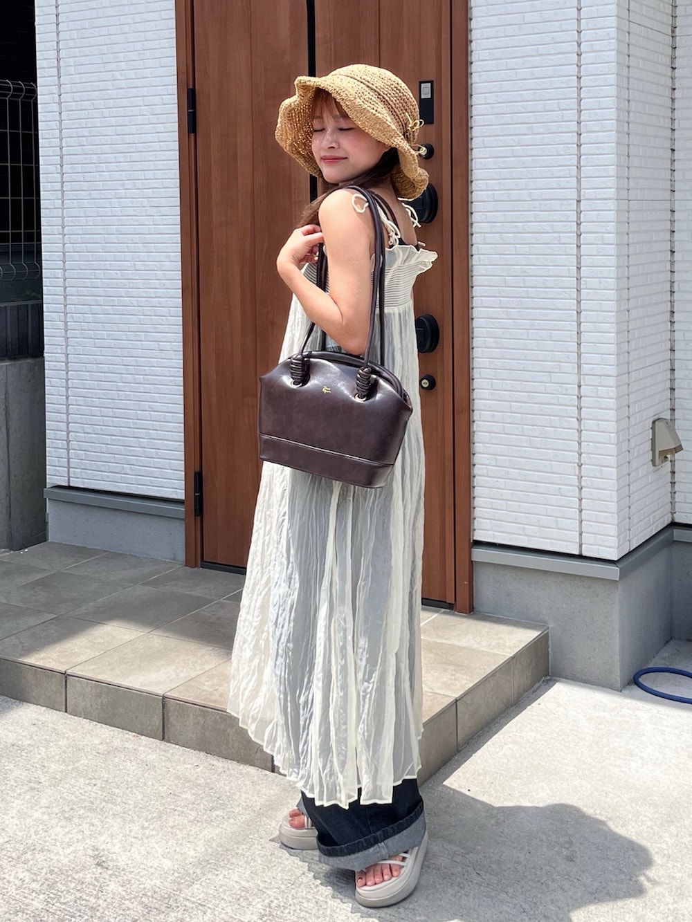 ブラウン系のショルダーバッグ、ホワイト系のワンピース、ブラック系のデニムパンツを着用したレディースの夏コーディネートの2枚目の写真