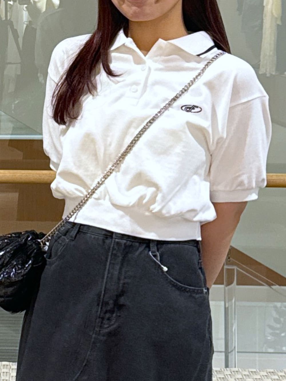 ホワイト系のポロシャツ、ブラック系のショルダーバッグ、ブラック系のデニムスカートを着用したレディースの春コーディネートの4枚目の写真