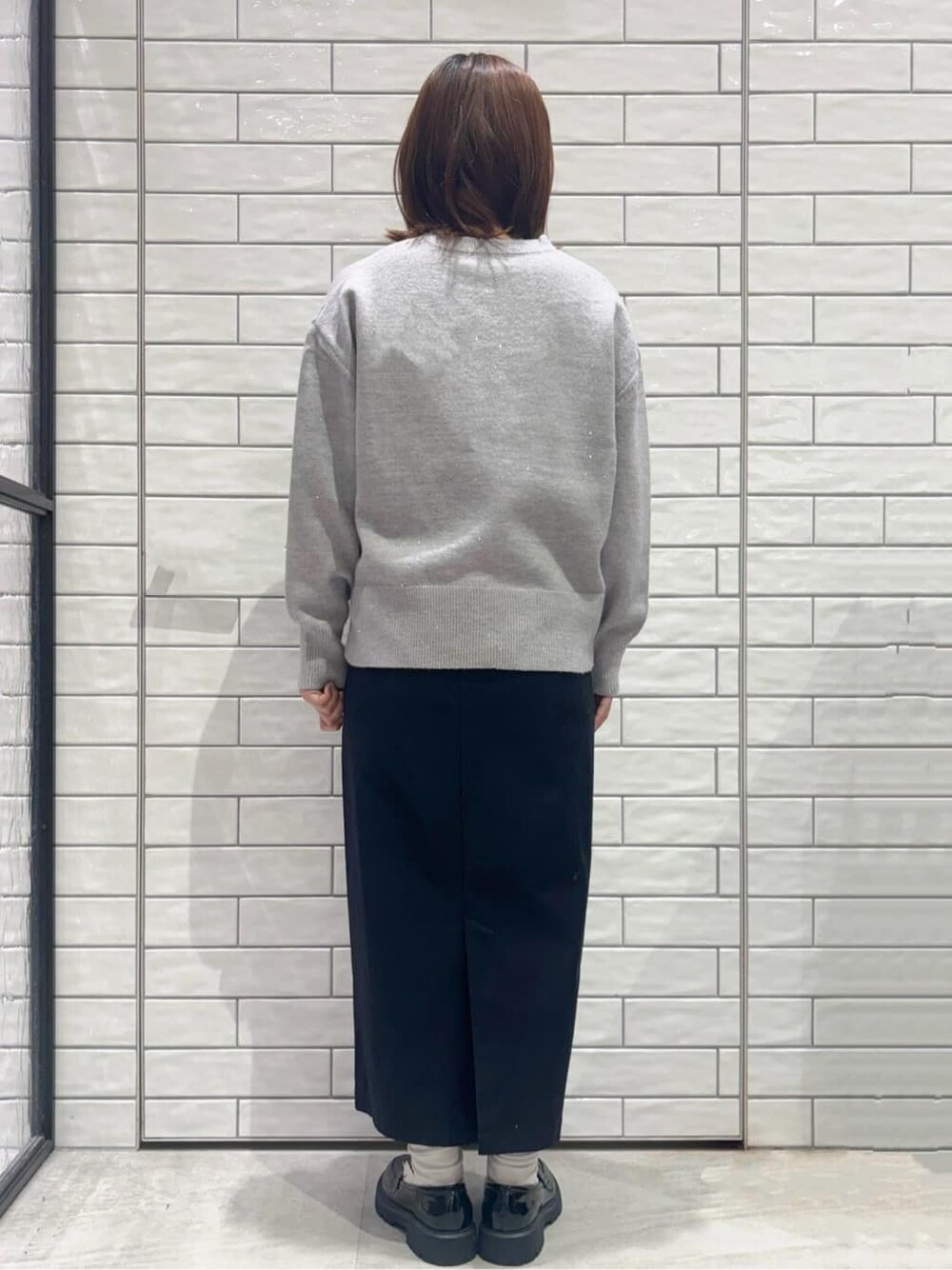 グレー系のニット/セーター、ブラック系のスカート、レッド系のハンドバッグを着用したレディースの冬コーディネートの3枚目の写真