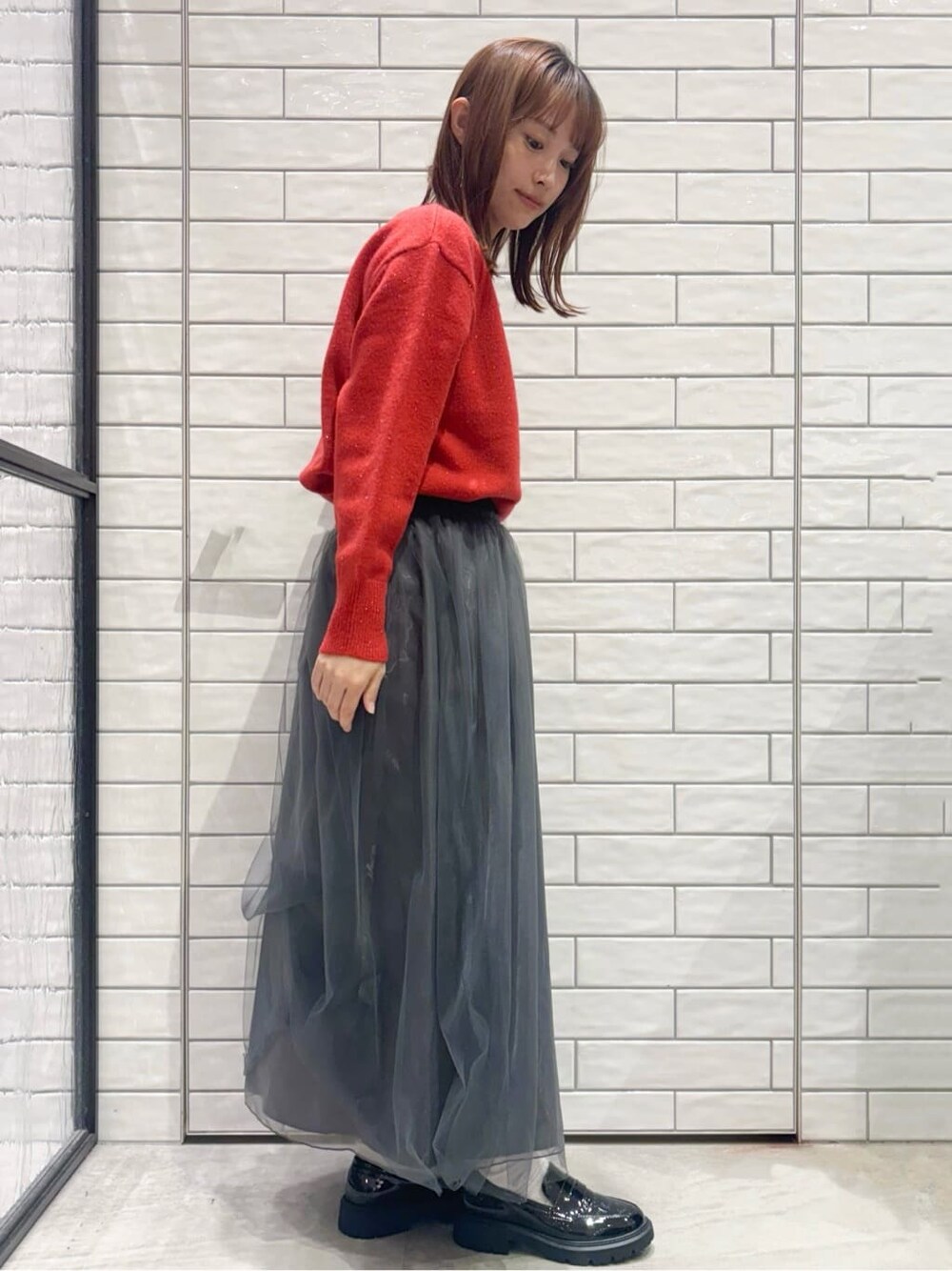 レッド系のニット/セーター、グレー系のスカート、シルバー系のショルダーバッグを着用したレディースの冬コーディネートの2枚目の写真