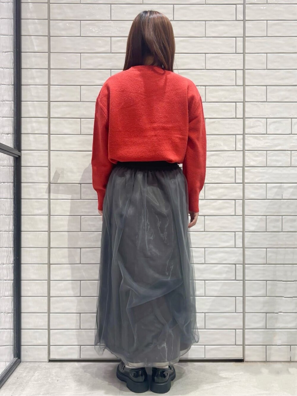 レッド系のニット/セーター、グレー系のスカート、シルバー系のショルダーバッグを着用したレディースの冬コーディネートの3枚目の写真