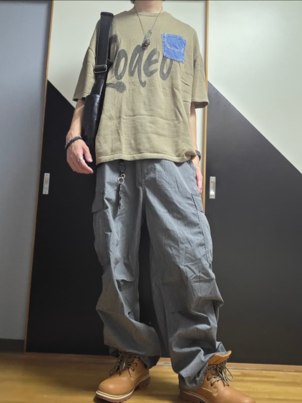 グレー系のカーゴパンツ、グレー系のショルダーバッグ、グリーン系のニット/セーターを着用したメンズの夏コーディネートの2枚目の写真