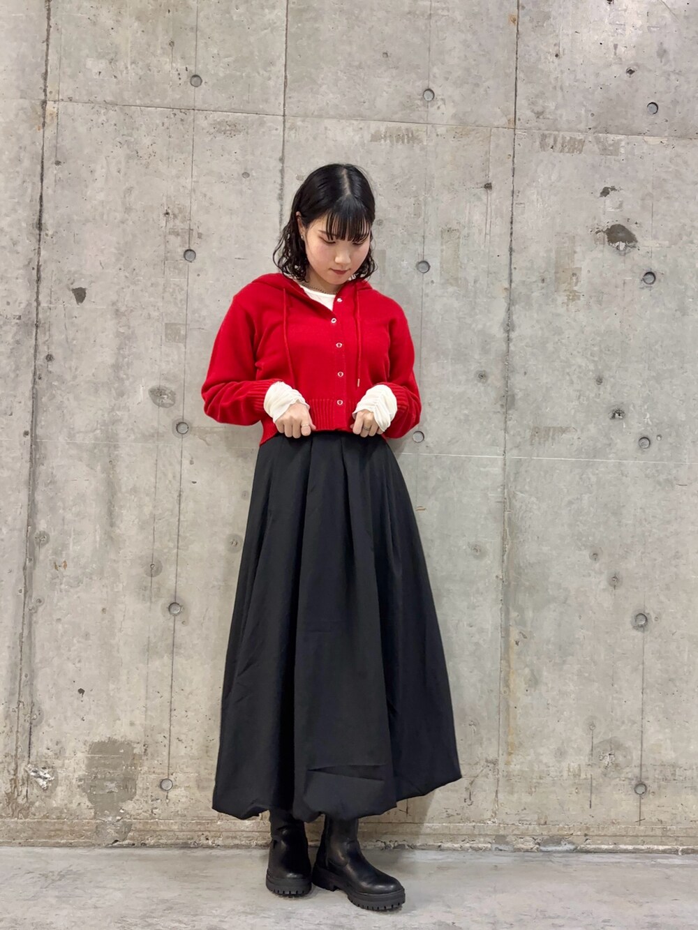ブラック系のスカート、レッド系のニット/セーター、ブラック系のブーツを着用したレディースの冬コーディネートの2枚目の写真