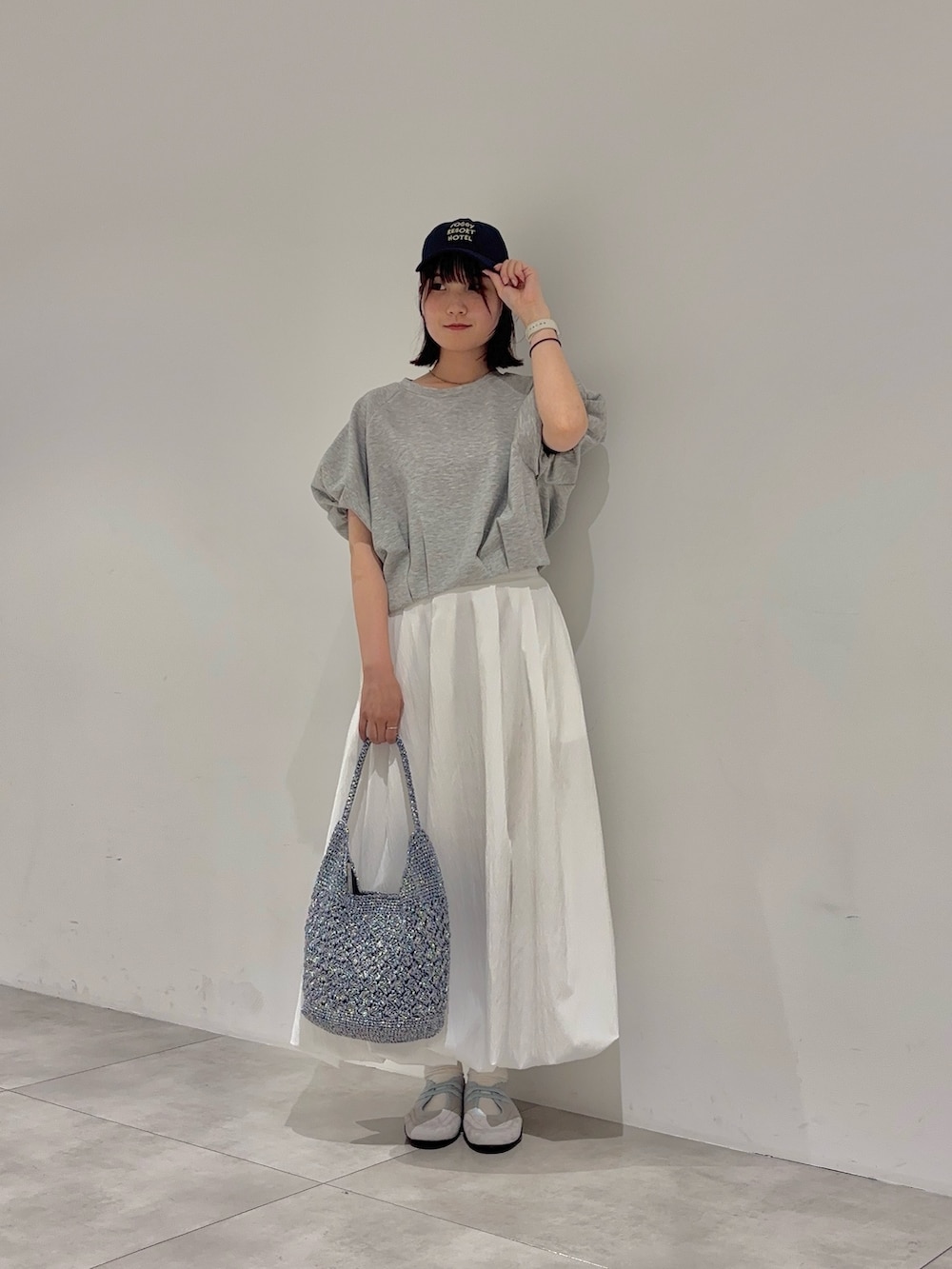 ホワイト系のスカート、ブルー系のかごバッグ、グレー系のTシャツ/カットソーを着用したレディースの夏コーディネートの2枚目の写真