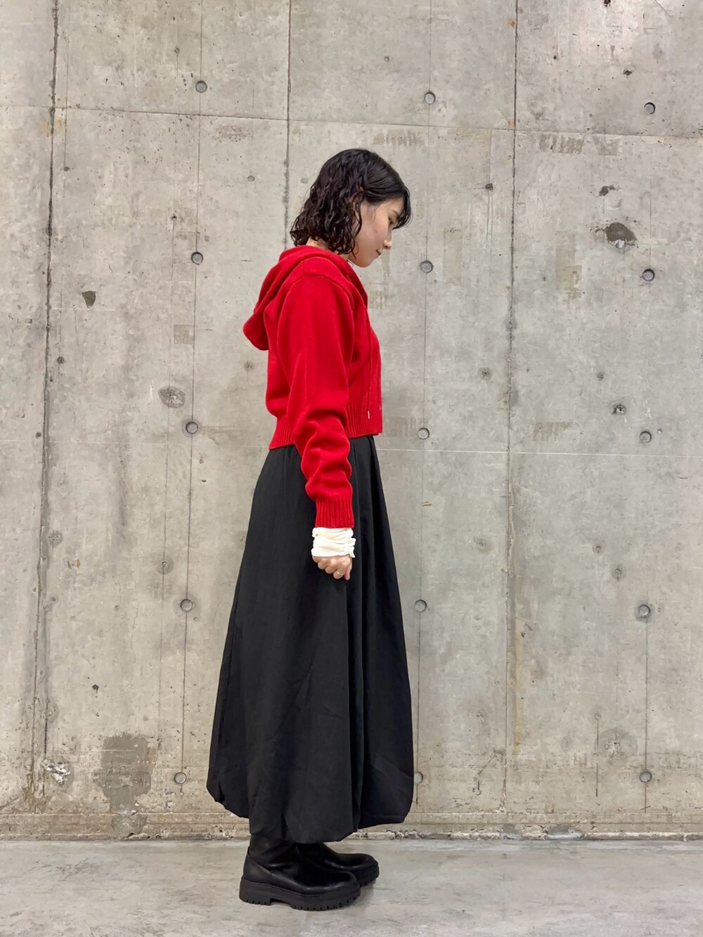 ブラック系のスカート、レッド系のニット/セーター、ブラック系のブーツを着用したレディースの冬コーディネートの3枚目の写真