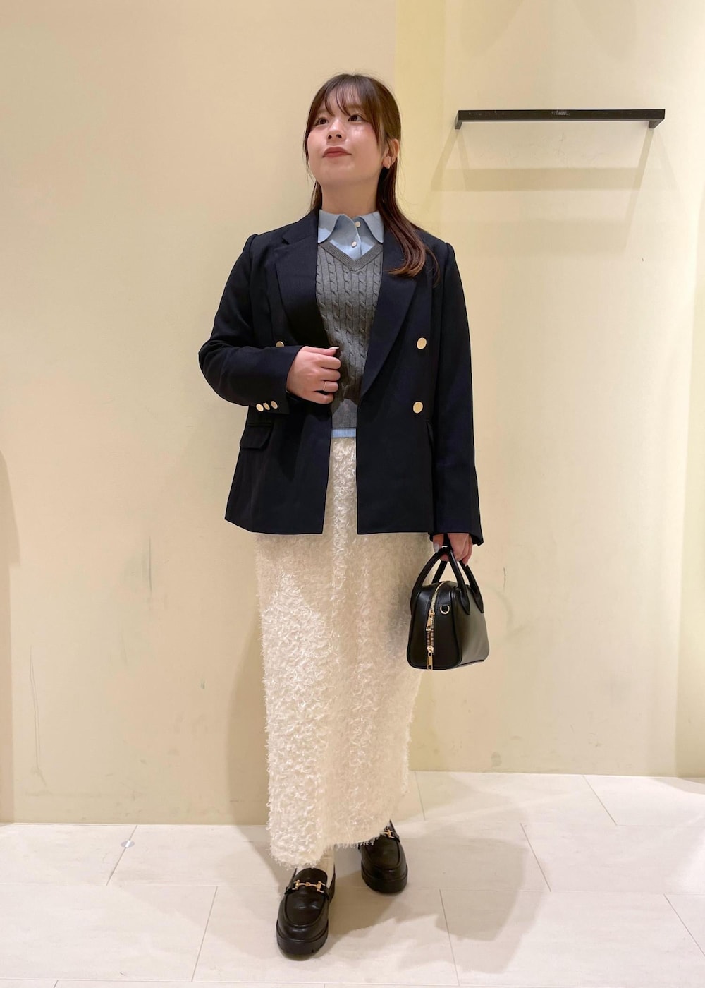 ブラック系のショルダーバッグ、ホワイト系のスカート、ブラック系のローファーを着用したレディースの秋コーディネートの3枚目の写真