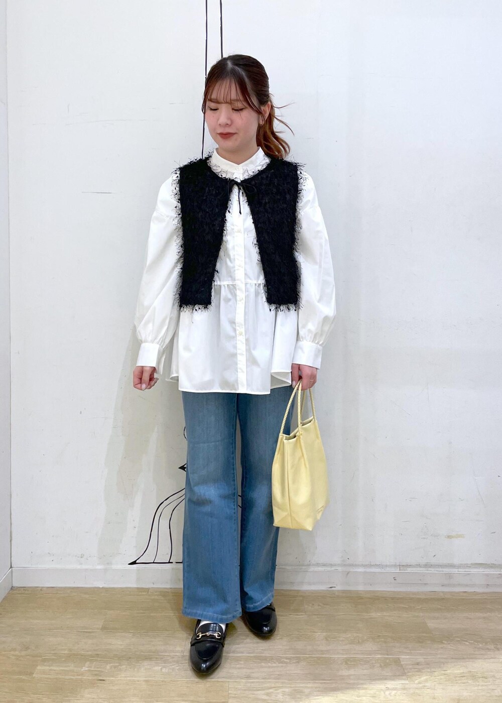 ブラック系のベスト、ブルー系のデニムパンツ、イエロー系のトートバッグを着用したレディースの冬コーディネートの4枚目の写真