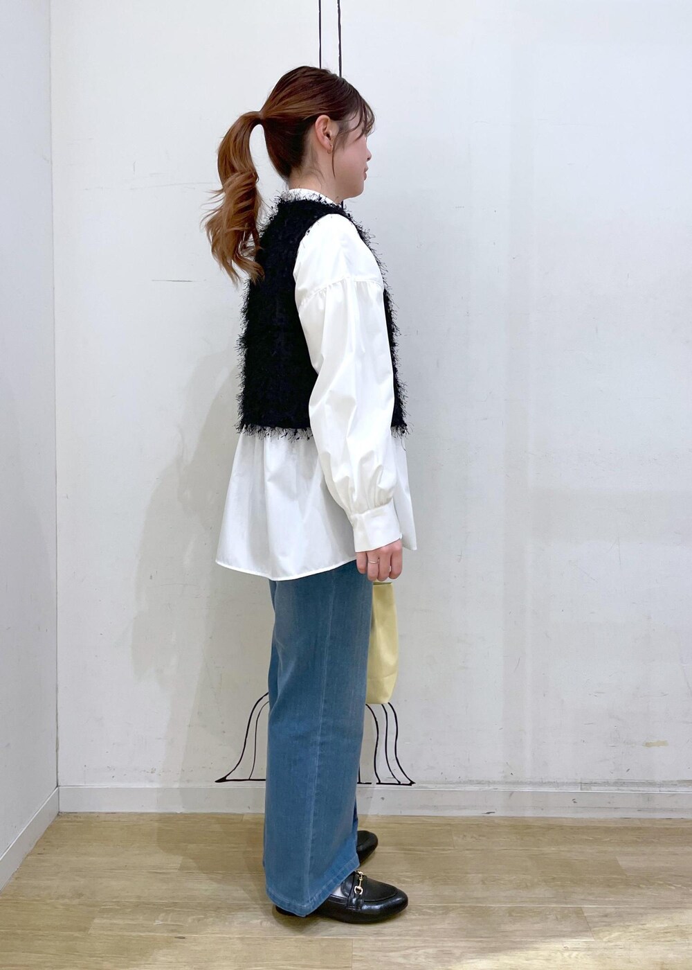ブラック系のベスト、ブルー系のデニムパンツ、イエロー系のトートバッグを着用したレディースの冬コーディネートの3枚目の写真