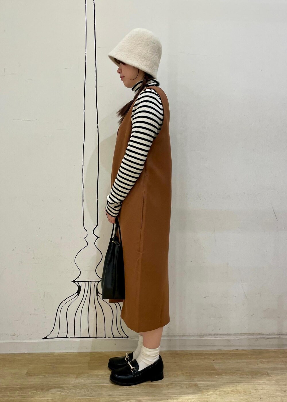 ホワイト系のニット/セーター、ブラウン系のジャンパースカート、ブラック系のローファーを着用したレディースの冬コーディネートの3枚目の写真