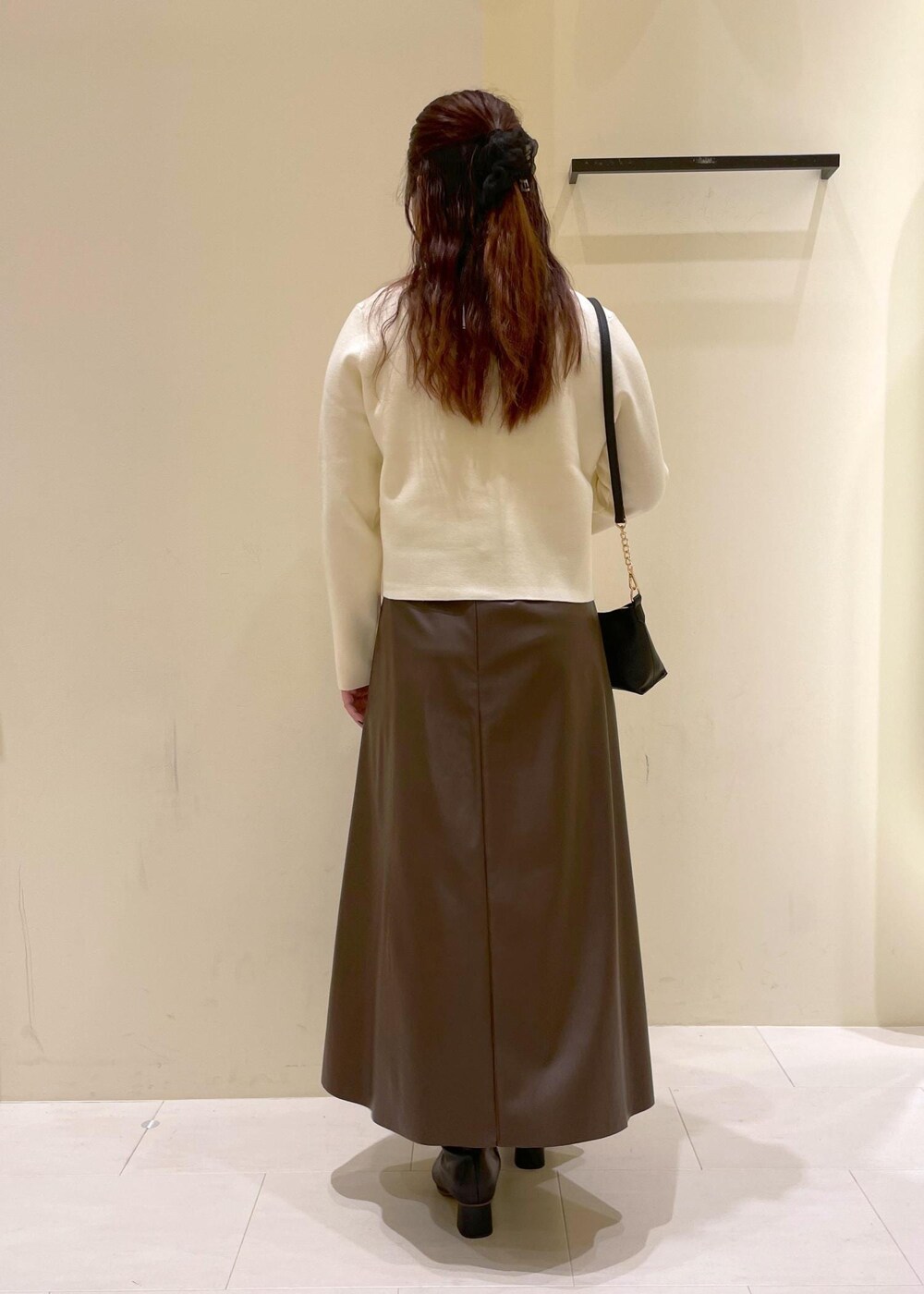 ブラック系のショルダーバッグ、ブラウン系のスカート、ホワイト系のカーディガン/ボレロを着用したレディースの秋コーディネートの2枚目の写真