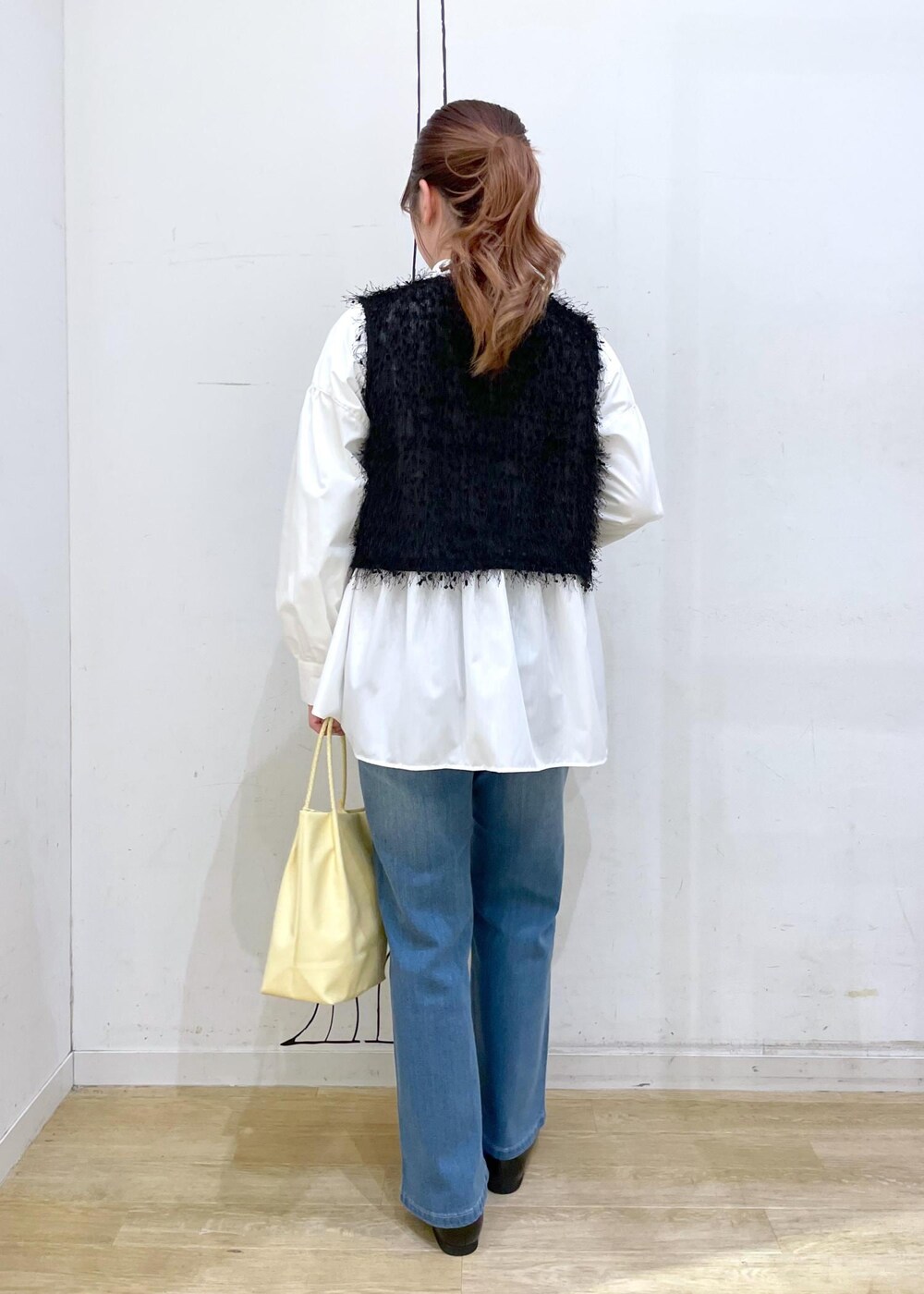 ブラック系のベスト、ブルー系のデニムパンツ、イエロー系のトートバッグを着用したレディースの冬コーディネートの2枚目の写真