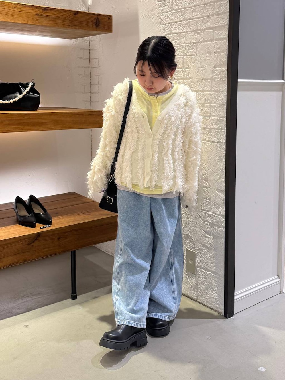 ブラック系のショルダーバッグ、イエロー系のTシャツ/カットソー、ブルー系のデニムパンツを着用したレディースの冬コーディネートの3枚目の写真