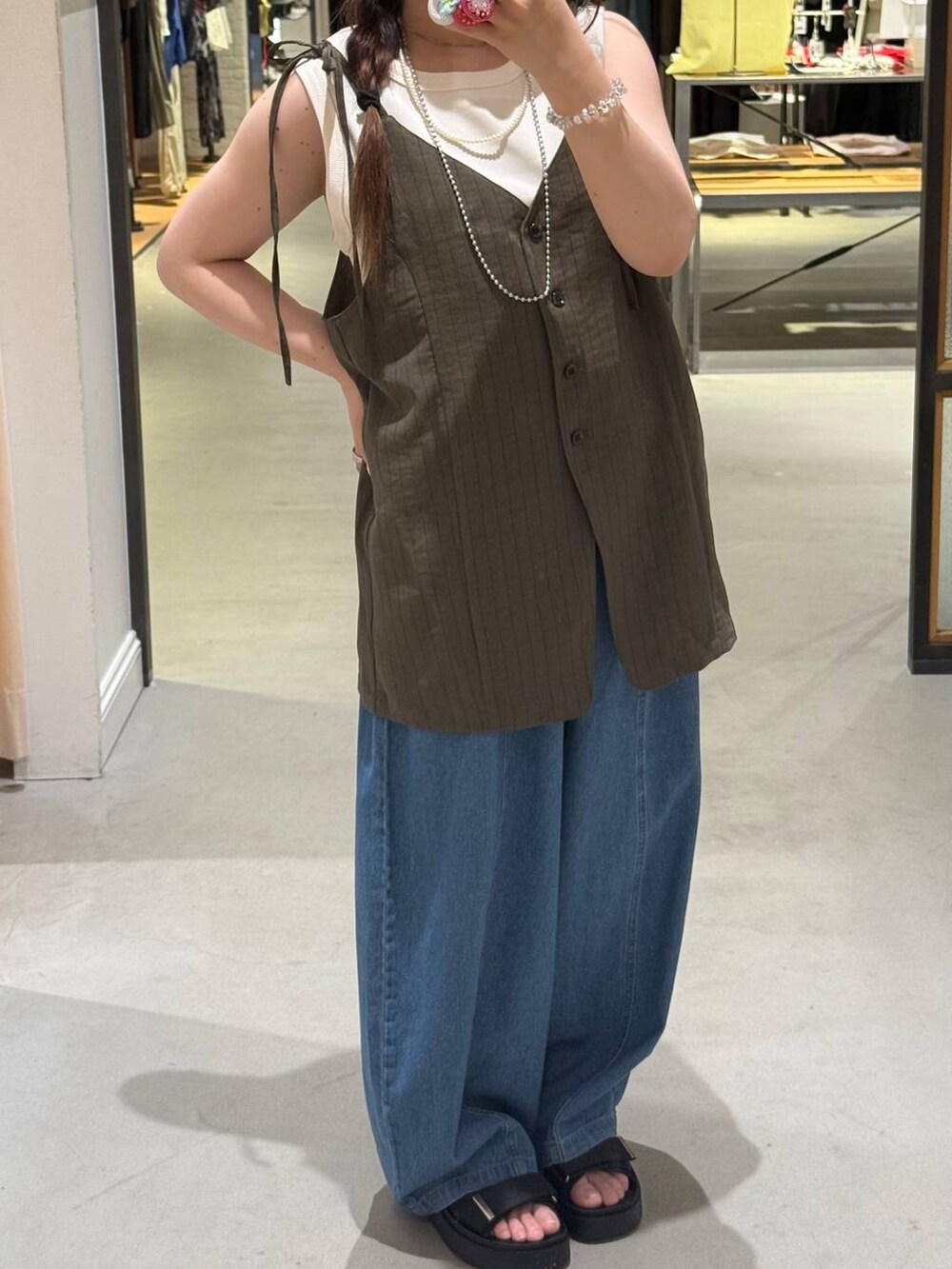 ホワイト系のタンクトップ、ブルー系のデニムパンツ、ブラック系のサンダルを着用したレディースの夏コーディネートの2枚目の写真