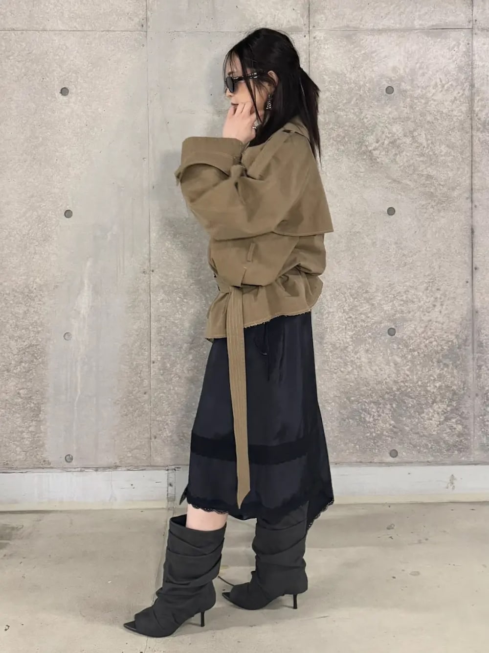 ベージュ系のトレンチコート、ブラック系のスカート、ブラック系のブーツを着用したレディースの春コーディネートの3枚目の写真