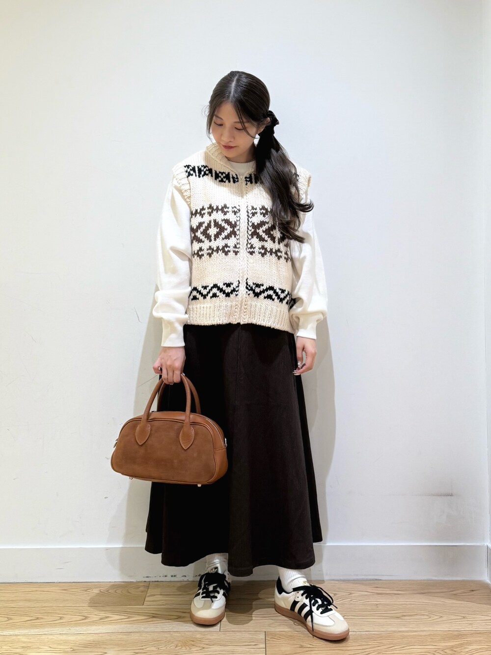 ホワイト系のベスト、ホワイト系のニット/セーター、ブラウン系のスカートを着用したレディースの秋コーディネートの2枚目の写真