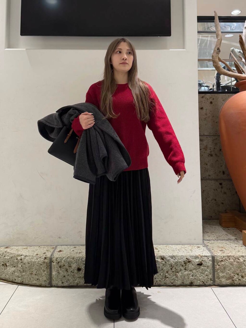 ブラック系のハンドバッグ、ブラウン系のブーツ、レッド系のニット/セーターを着用したレディースの冬コーディネートの5枚目の写真