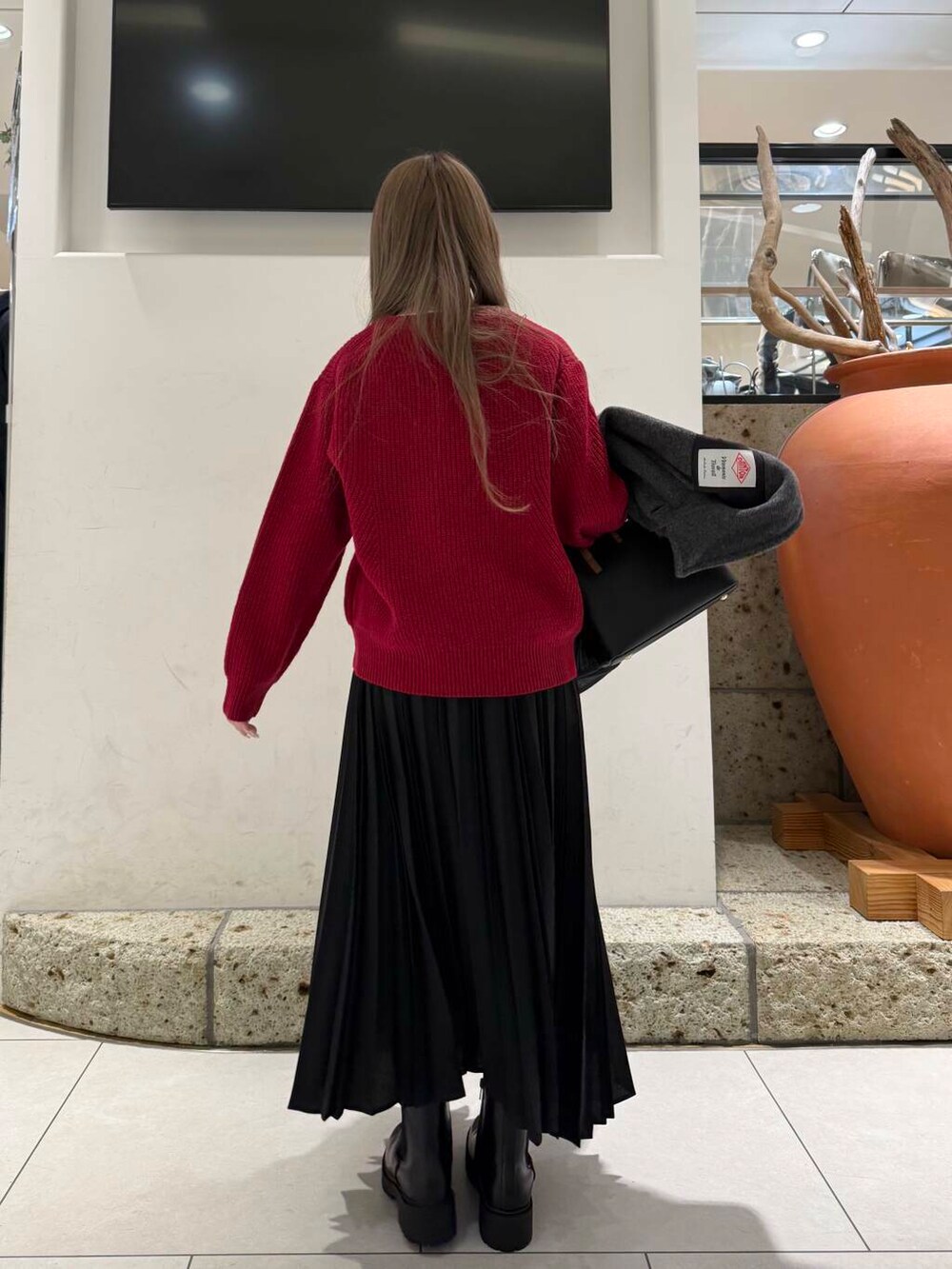 ブラック系のハンドバッグ、ブラウン系のブーツ、レッド系のニット/セーターを着用したレディースの冬コーディネートの6枚目の写真