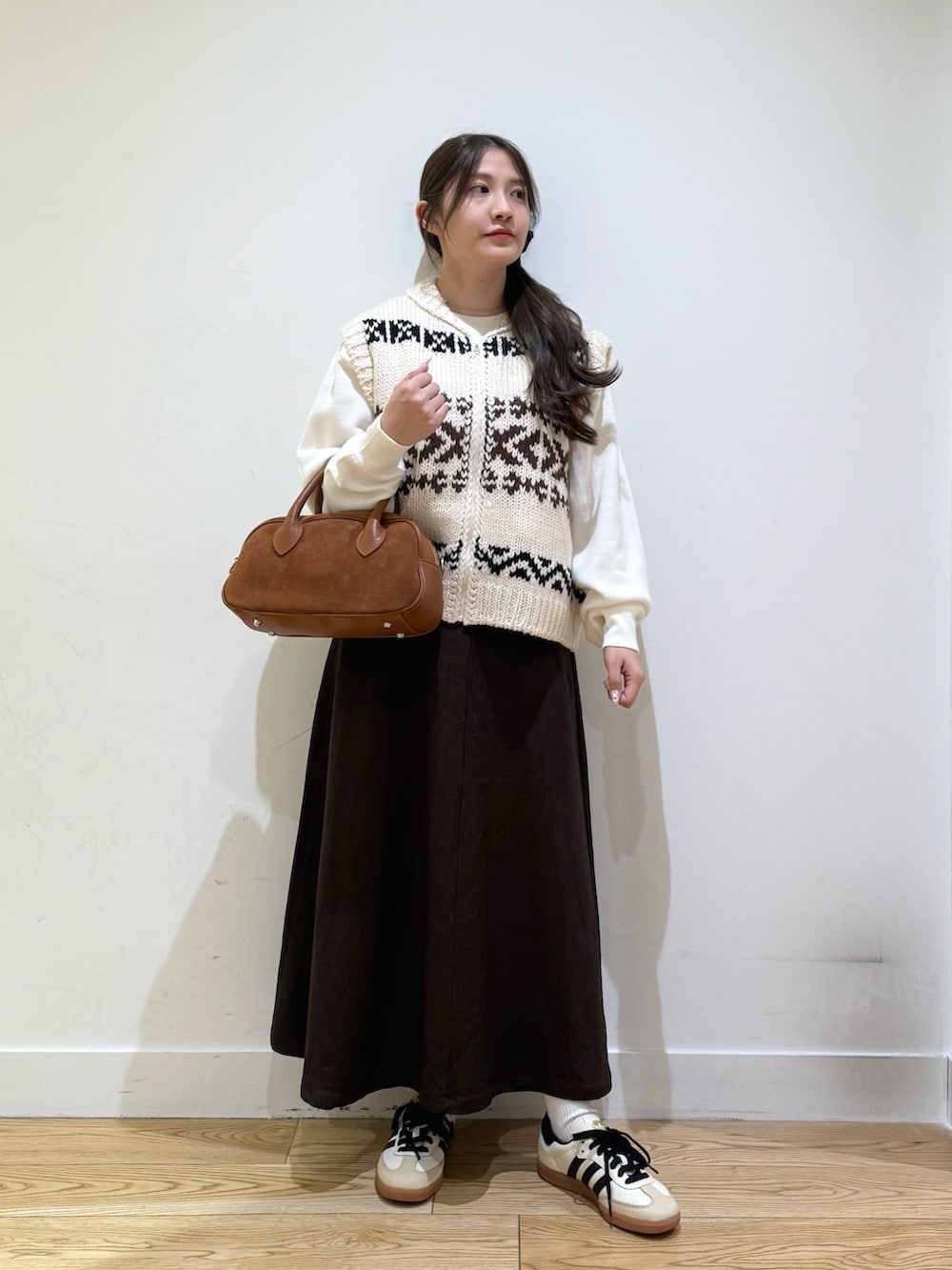 ホワイト系のベスト、ホワイト系のニット/セーター、ブラウン系のスカートを着用したレディースの秋コーディネートの3枚目の写真
