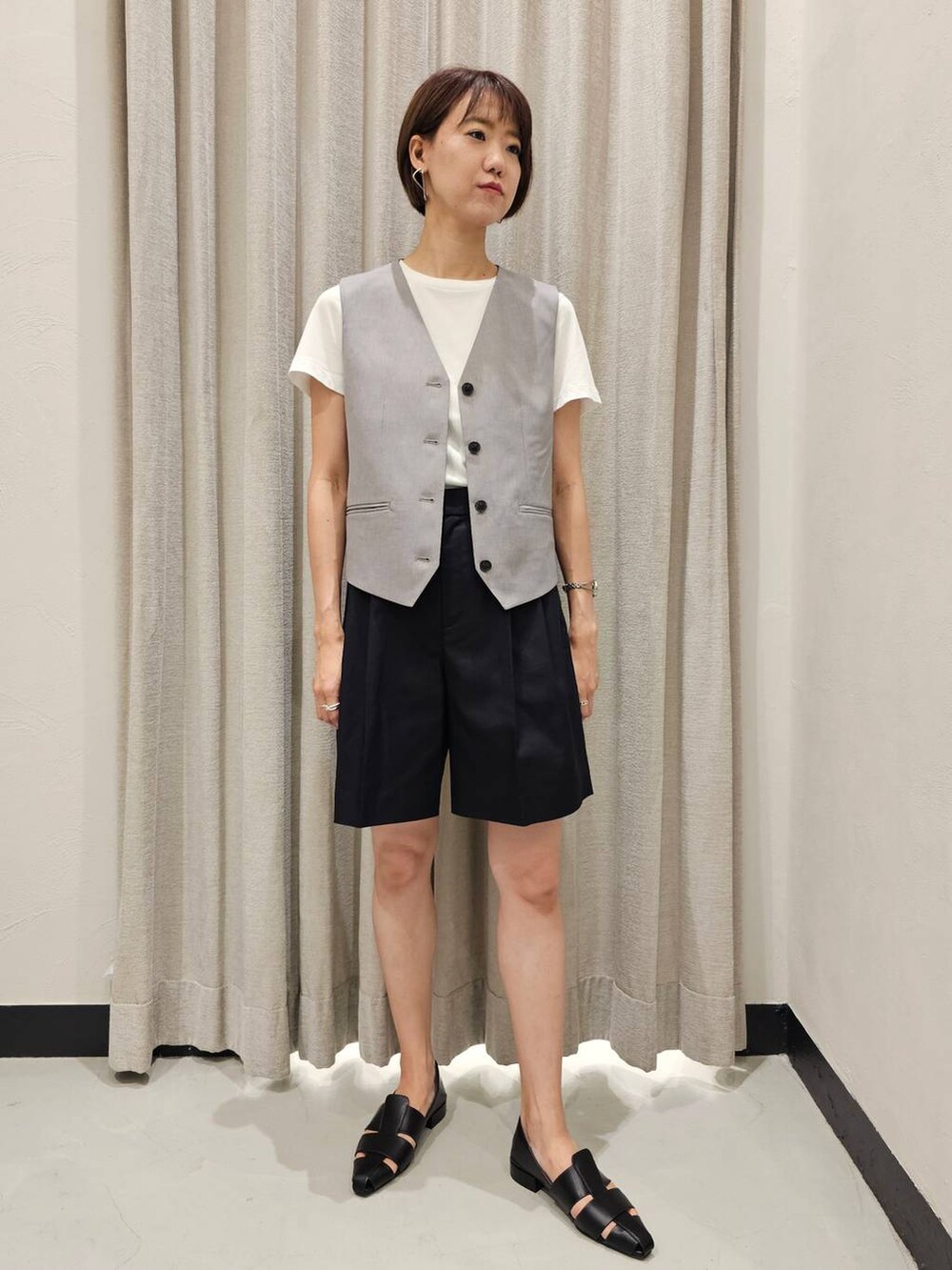 グレー系のベスト、ブラック系のチノパンツ、ブラック系のパンプスを着用したレディースの夏コーディネートの5枚目の写真