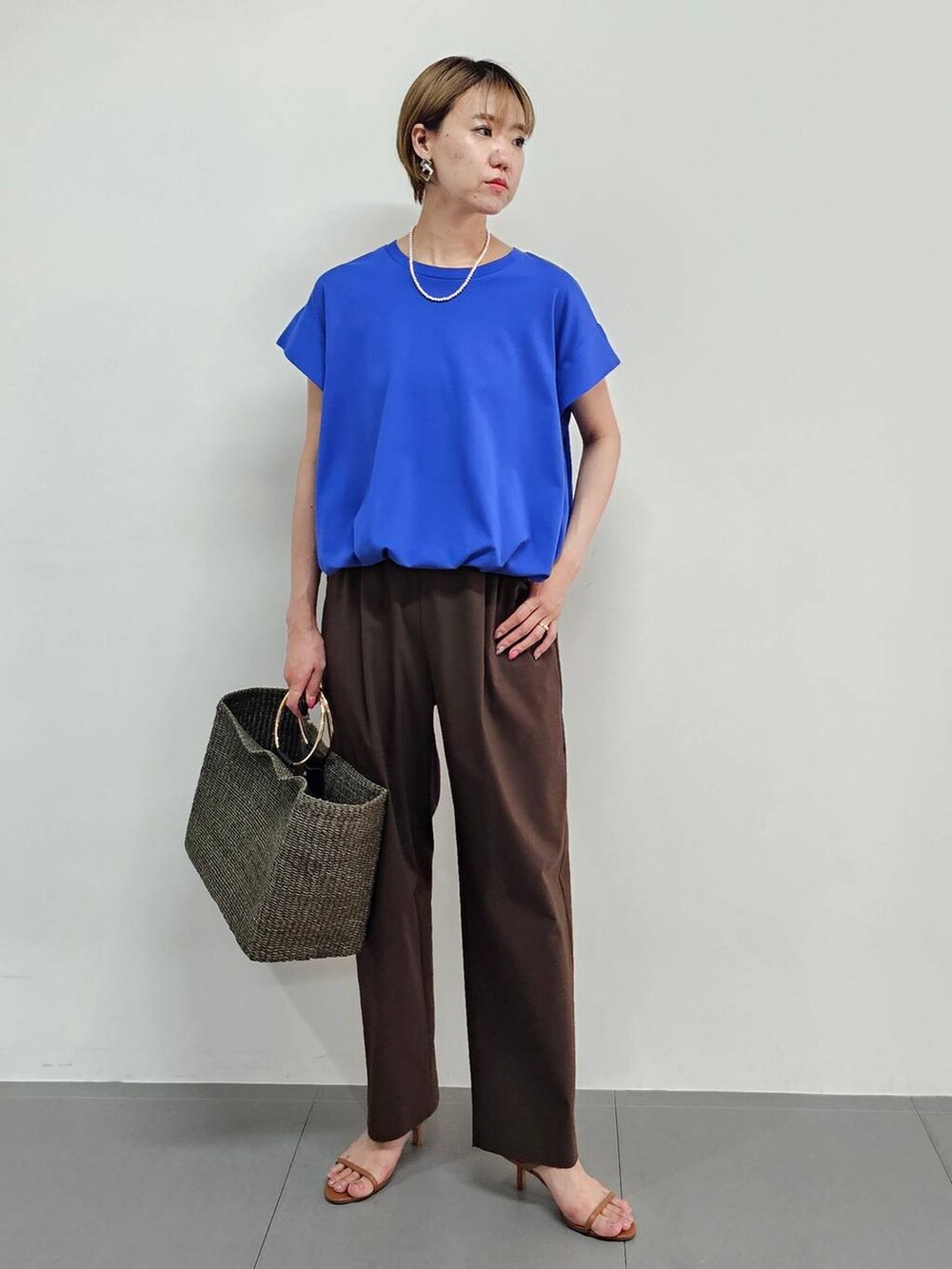 ブラウン系のかごバッグ、ブルー系のTシャツ/カットソー、ブラウン系のサンダルを着用したレディースの夏コーディネートの5枚目の写真