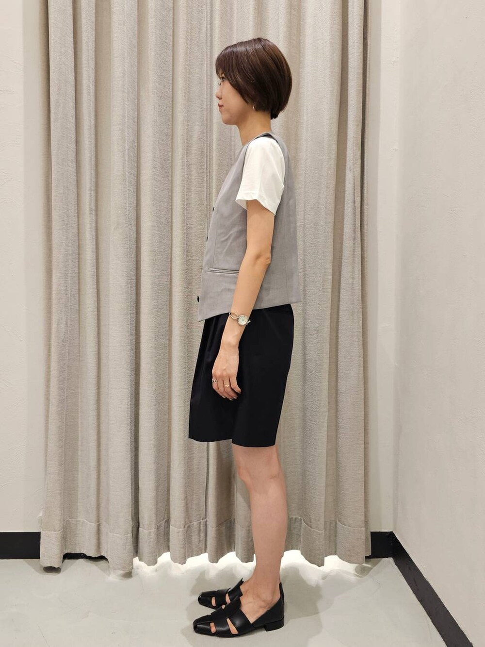 グレー系のベスト、ブラック系のチノパンツ、ブラック系のパンプスを着用したレディースの夏コーディネートの4枚目の写真