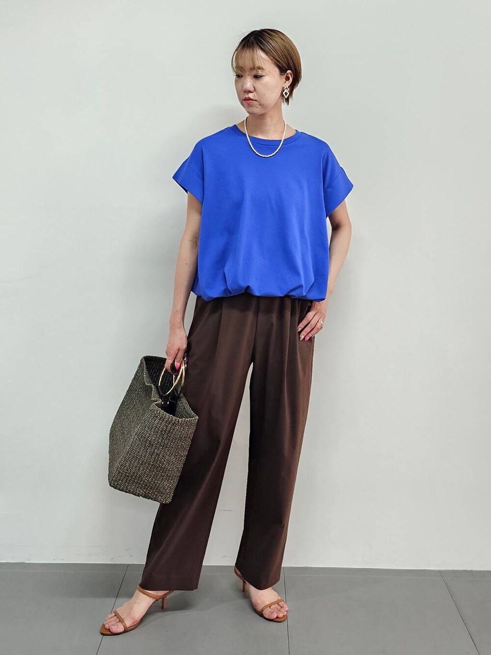 ブラウン系のかごバッグ、ブルー系のTシャツ/カットソー、ブラウン系のサンダルを着用したレディースの夏コーディネートの2枚目の写真