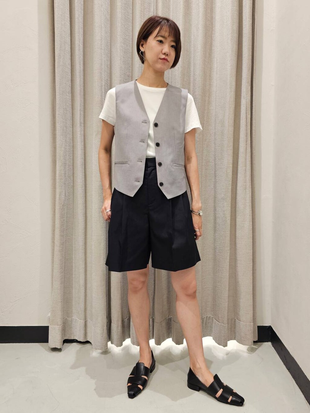 グレー系のベスト、ブラック系のチノパンツ、ブラック系のパンプスを着用したレディースの夏コーディネートの2枚目の写真