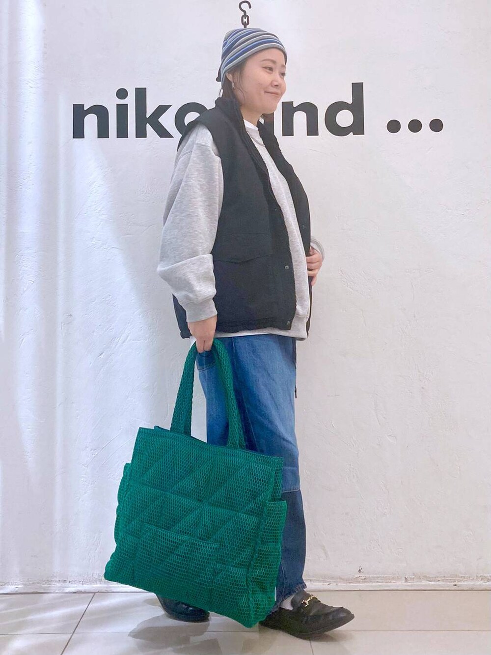 グリーン系のトートバッグ、ブルー系のデニムパンツ、ブラック系のベストを着用したレディースの冬コーディネートの5枚目の写真