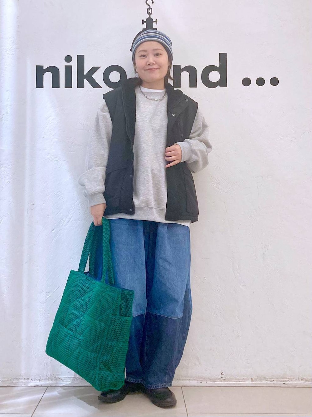 グリーン系のトートバッグ、ブルー系のデニムパンツ、ブラック系のベストを着用したレディースの冬コーディネートの2枚目の写真