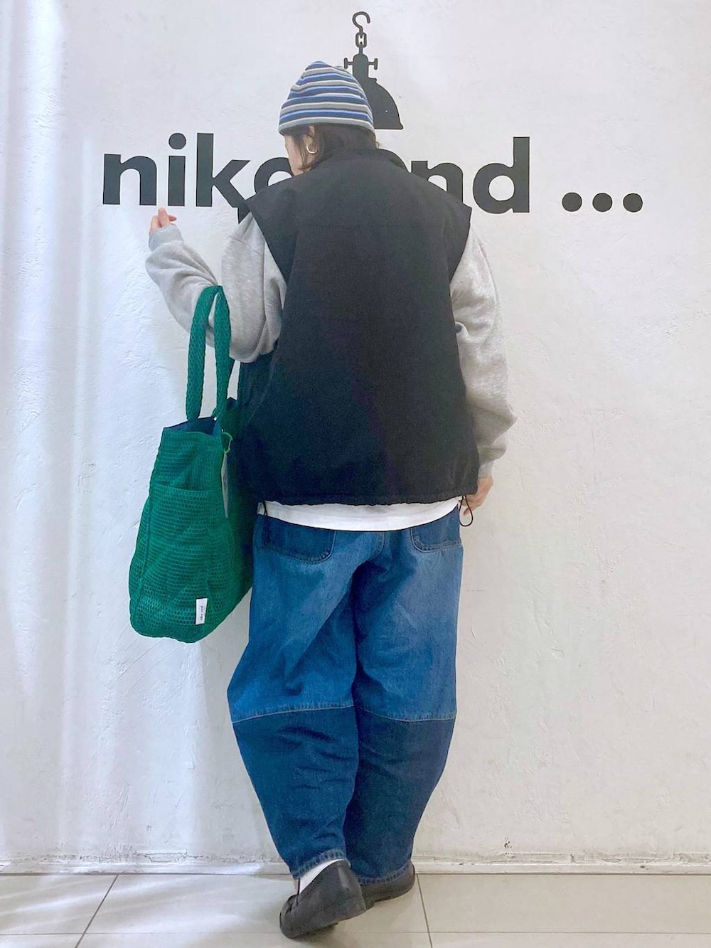 グリーン系のトートバッグ、ブルー系のデニムパンツ、ブラック系のベストを着用したレディースの冬コーディネートの4枚目の写真