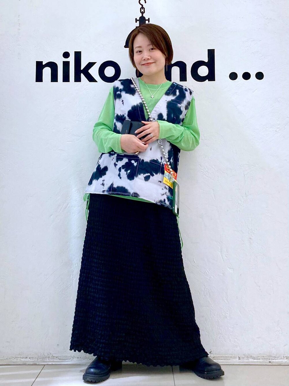 ブルー系のベスト、ブラック系のスカート、グリーン系のTシャツ/カットソーを着用したレディースの春コーディネートの2枚目の写真