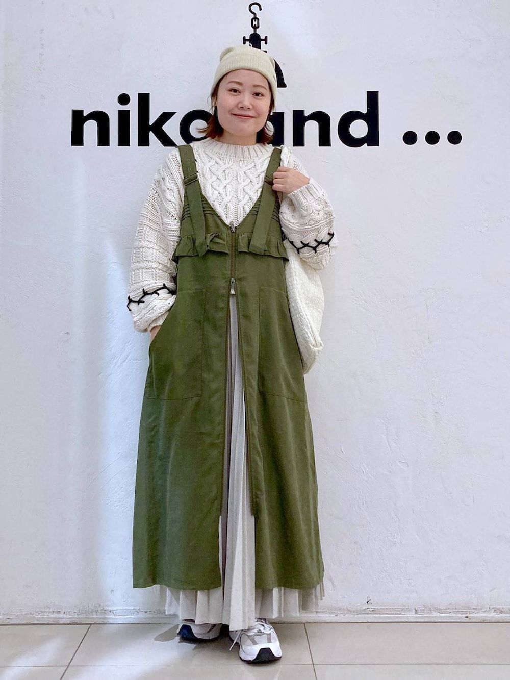 グリーン系のジャンパースカート、ベージュ系のショルダーバッグ、ベージュ系のニット/セーターを着用したレディースの冬コーディネートの2枚目の写真