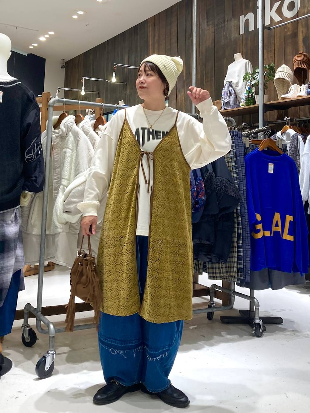 ブルー系のデニムパンツ、ブラウン系のショルダーバッグ、イエロー系のワンピースを着用したレディースの秋コーディネートの2枚目の写真