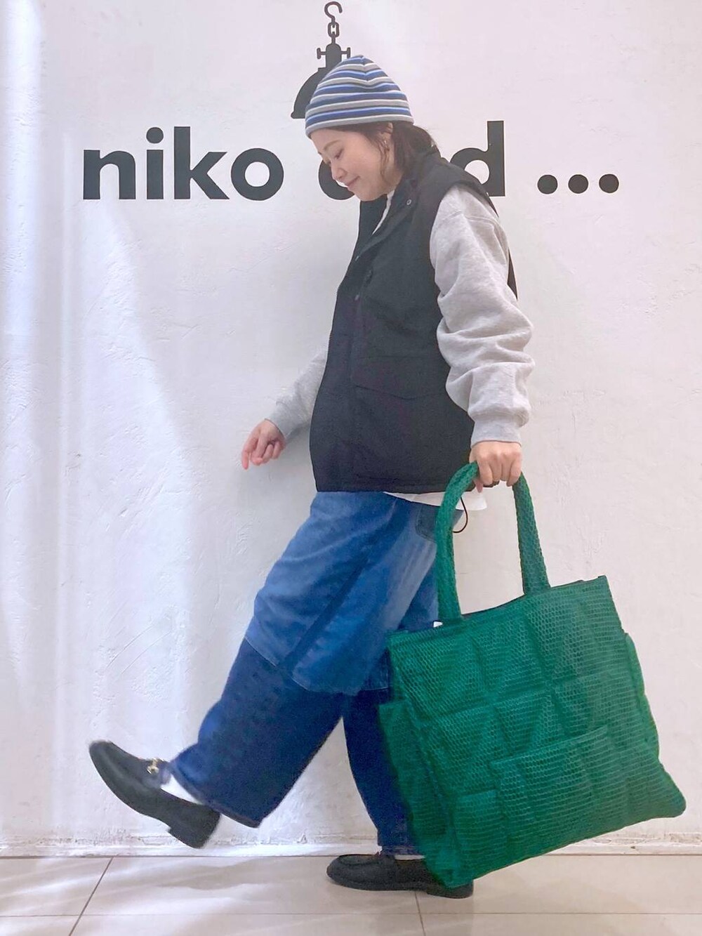 グリーン系のトートバッグ、ブルー系のデニムパンツ、ブラック系のベストを着用したレディースの冬コーディネートの3枚目の写真