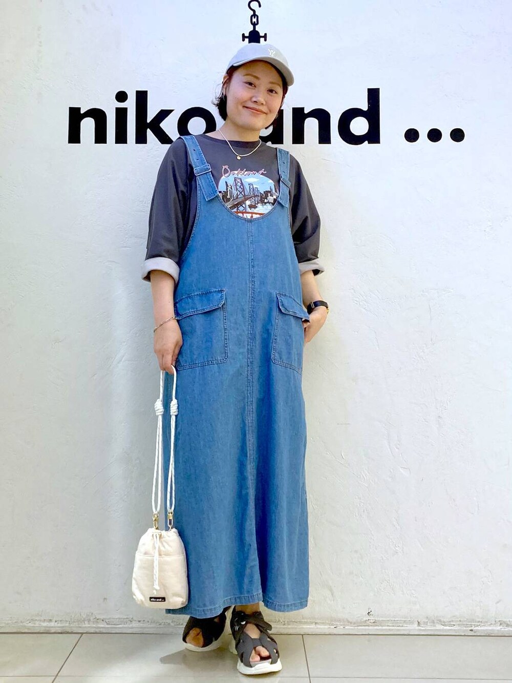 ホワイト系のショルダーバッグ、グレー系のTシャツ/カットソー、ブルー系のジャンパースカートを着用したレディースの夏コーディネートの2枚目の写真