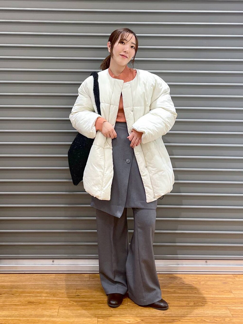 オレンジ系のニット/セーター、ブラウン系のブーツ、ブラック系のショルダーバッグを着用したレディースの冬コーディネートの2枚目の写真