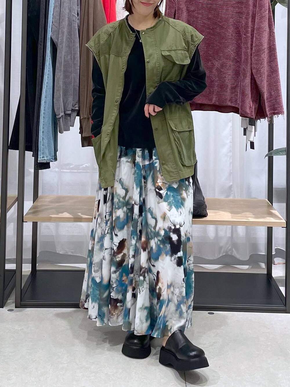 グリーン系のベスト、ブラック系のTシャツ/カットソー、ブルー系のスカートを着用したレディースの秋コーディネートの3枚目の写真