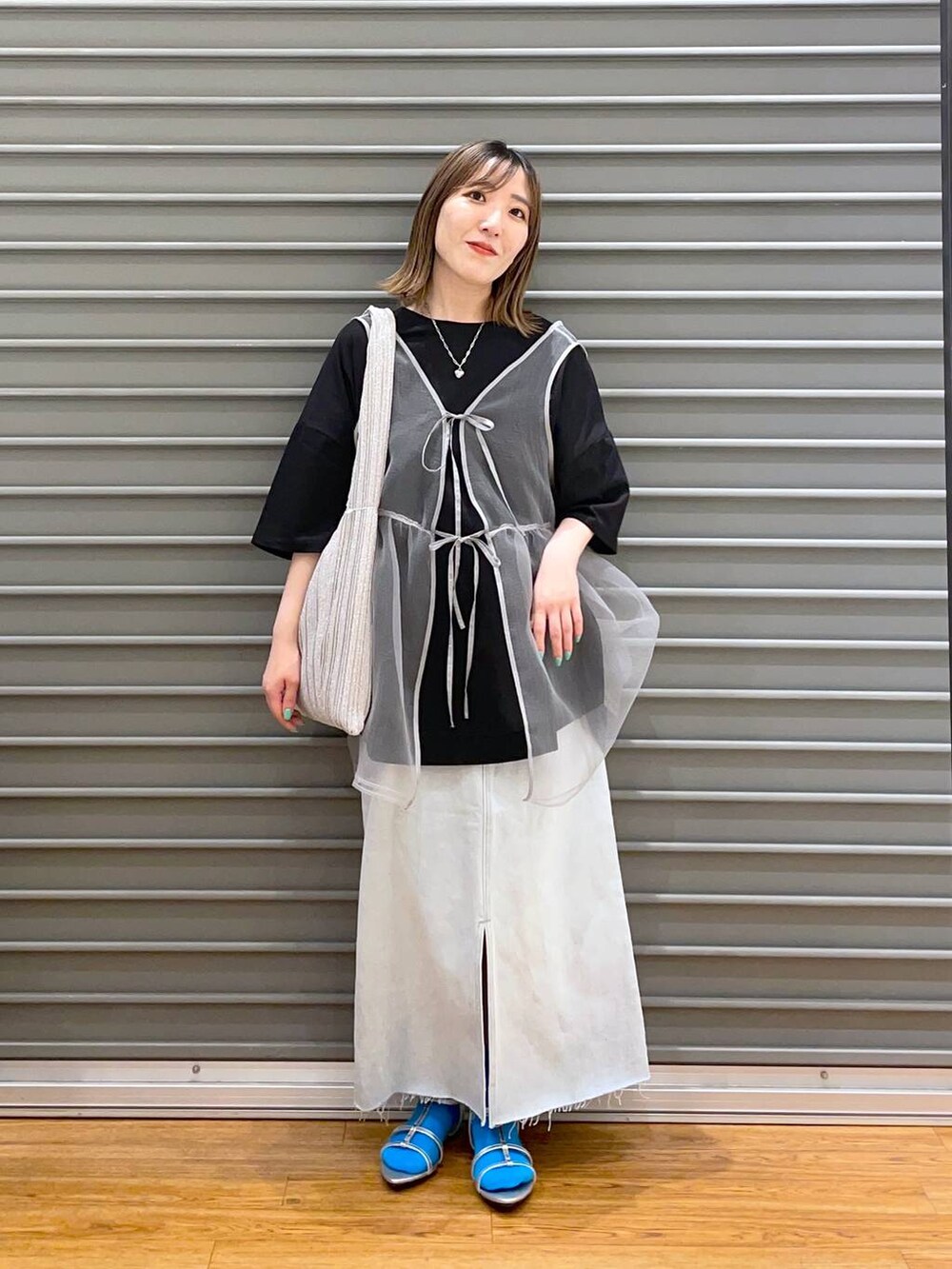 ブラック系のベスト、ブルー系のスカート、シルバー系のショルダーバッグを着用したレディースの春コーディネートの2枚目の写真