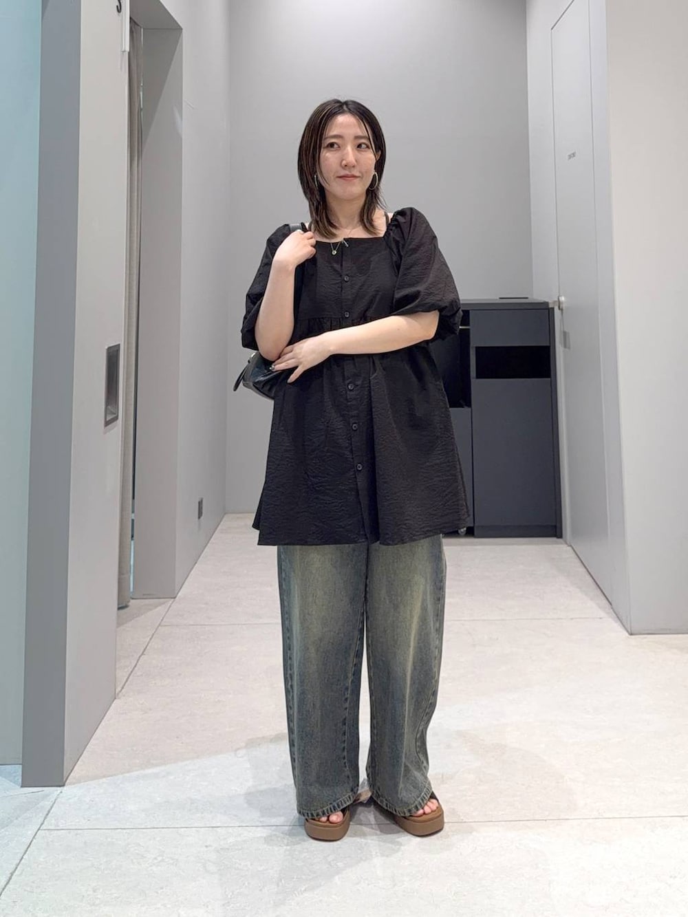 ブラック系のサンダル、ブルー系のデニムパンツ、ブラック系のショルダーバッグを着用したレディースの夏コーディネートの2枚目の写真