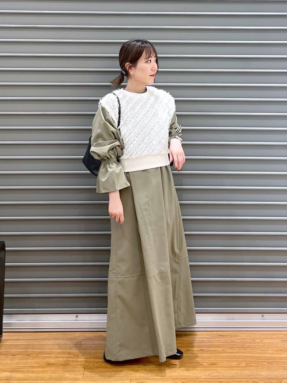 ホワイト系のベスト、ブラック系のパンプス、グリーン系のワンピースを着用したレディースの春コーディネートの2枚目の写真