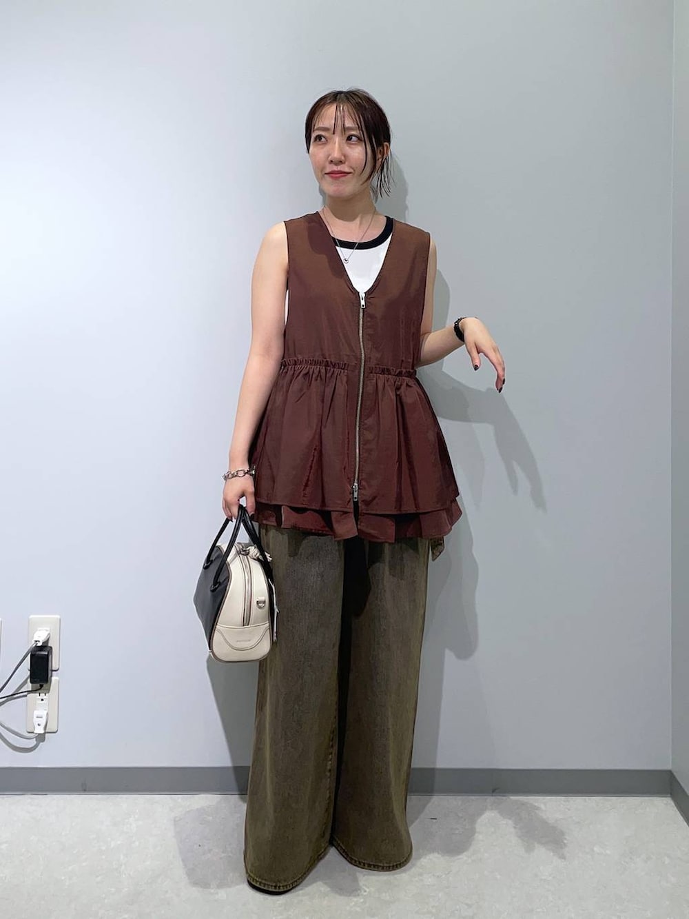 ブラウン系のベスト、ブラウン系のデニムパンツ、ブラック系のハンドバッグを着用したレディースの秋コーディネートの2枚目の写真