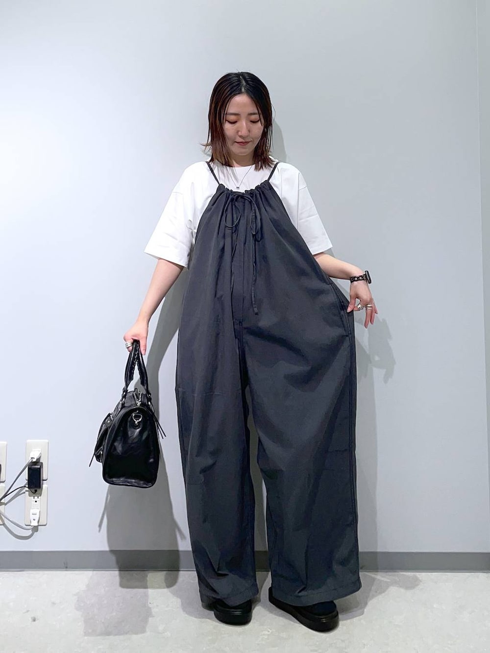 グレー系のサロペット/オーバーオール、ホワイト系のTシャツ/カットソー、ブラック系のサンダルを着用したレディースの春コーディネートの2枚目の写真