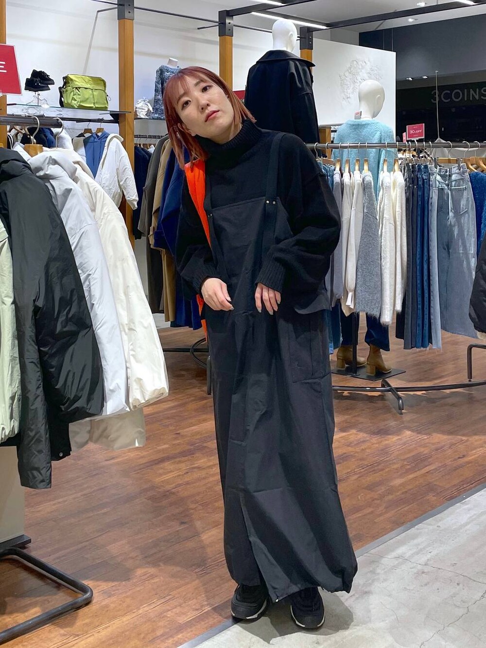 ブラック系のニット/セーター、オレンジ系のトートバッグ、グレー系のジャンパースカートを着用したレディースの冬コーディネートの2枚目の写真